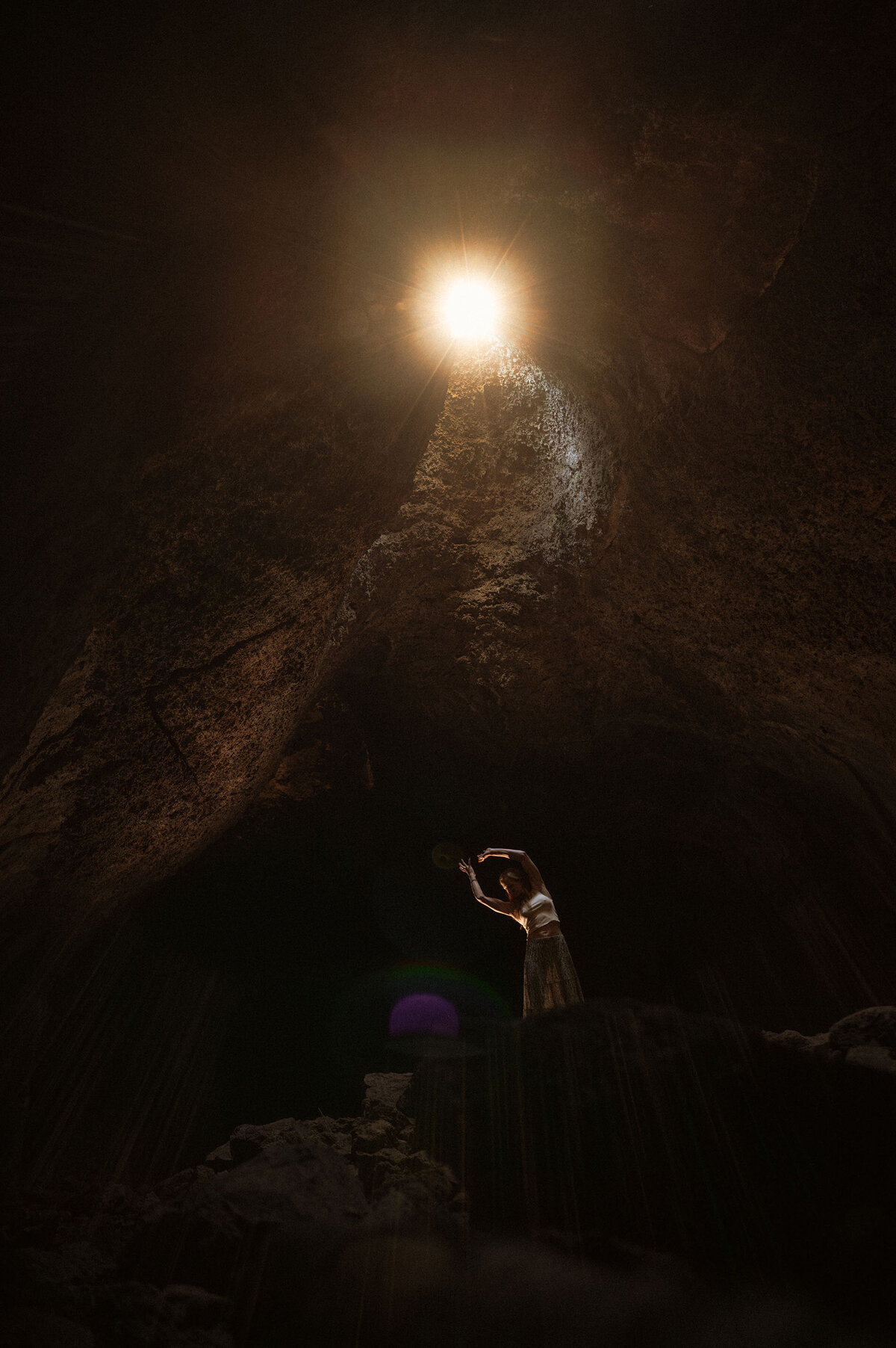 woman poses artistically in an Oregon cave as the light casts down on her creating shadows