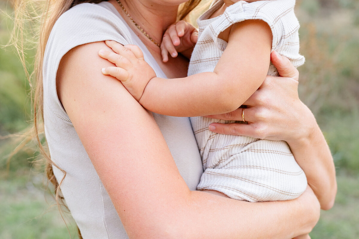 A touching close-up of a baby’s tiny hands grasping his mother’s arm, highlighting the warmth and love between them.