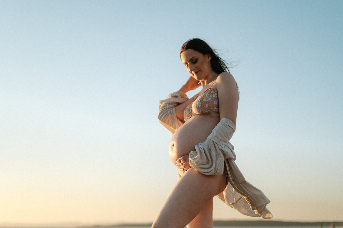 Artistic outdoor maternity photography of a woman holding her bump at sunset