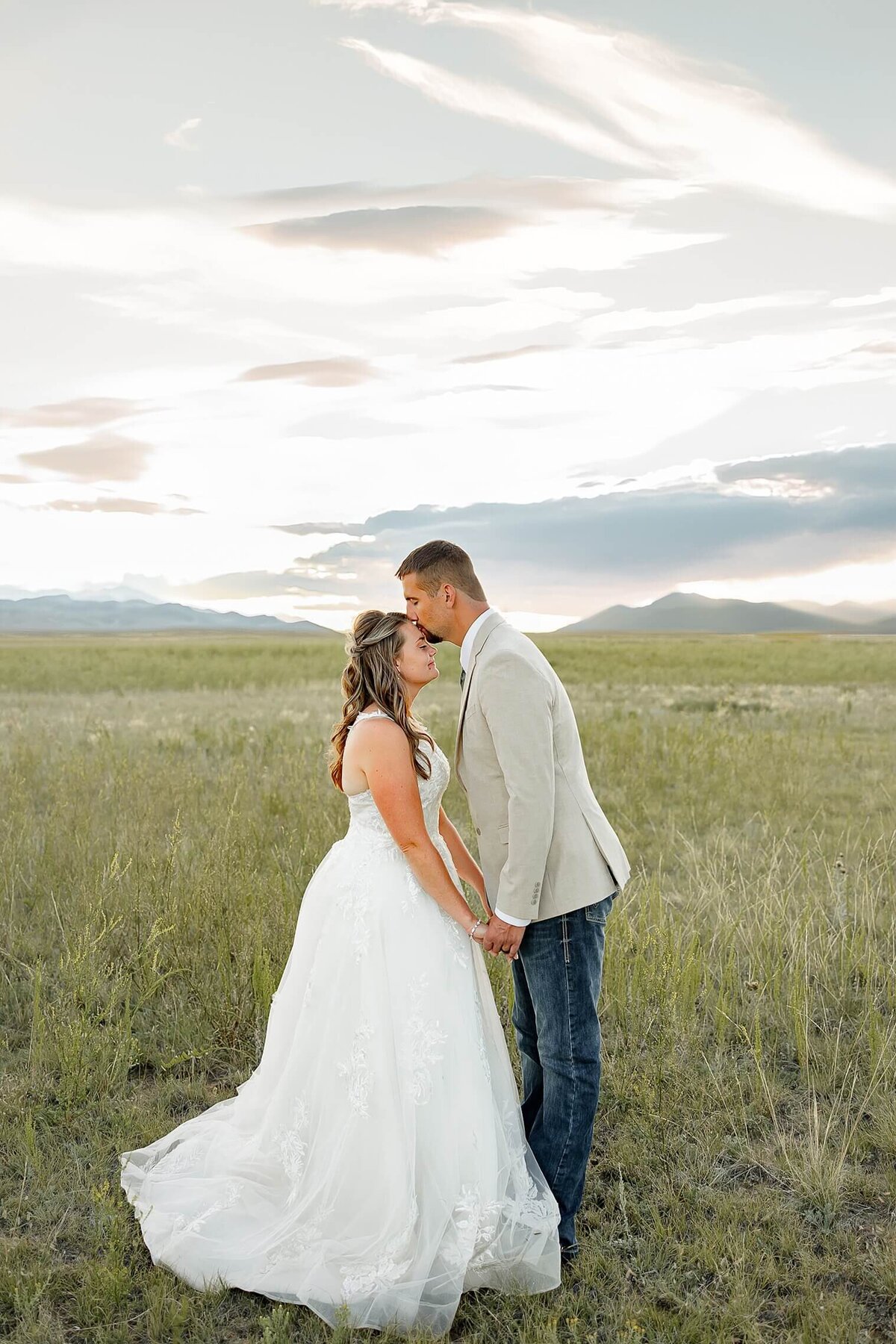 Wedding photography of groom kissing bride on her forhead and holding hands