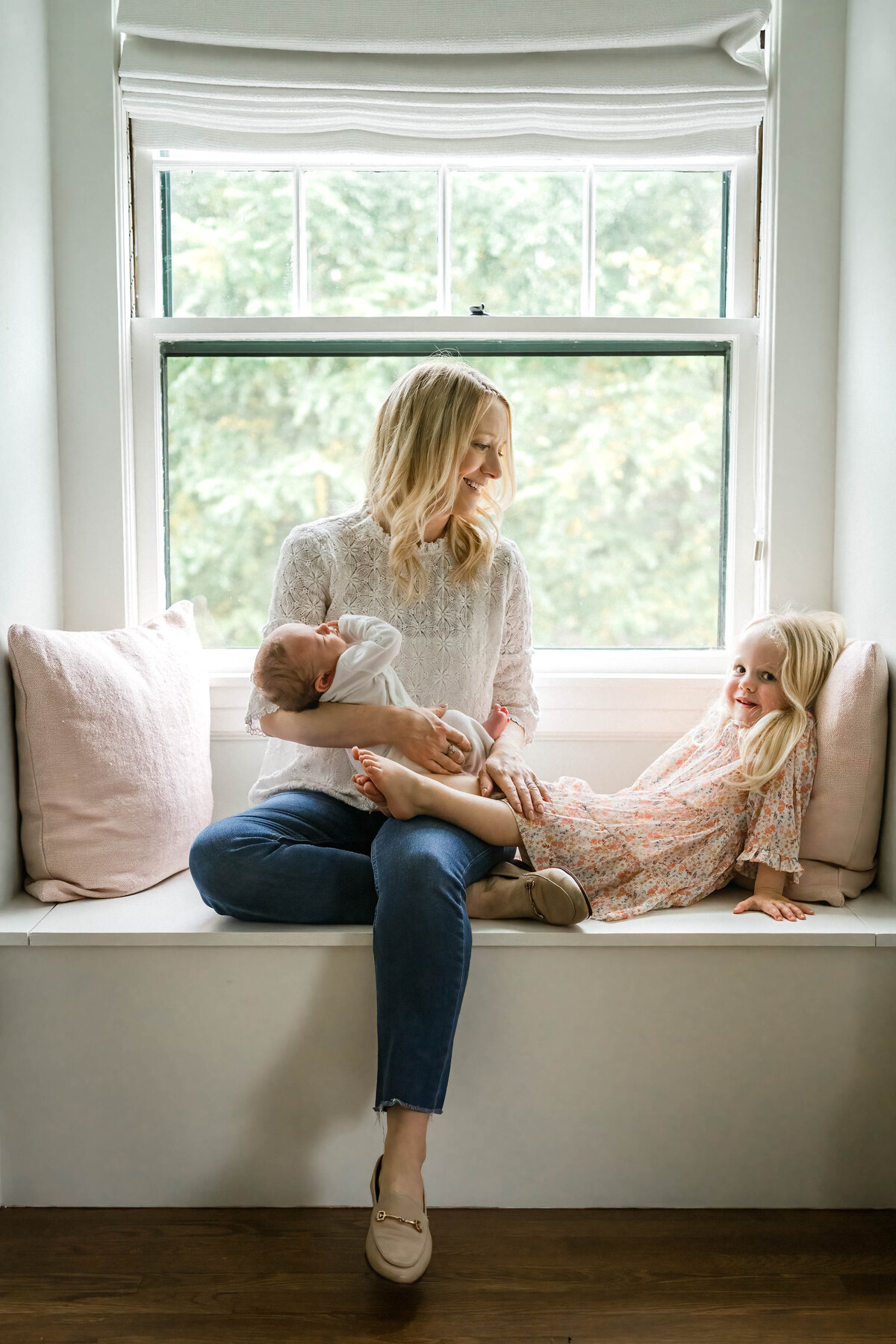 Mom sitting in window seat cradling newborn daughter sitting next to toddler