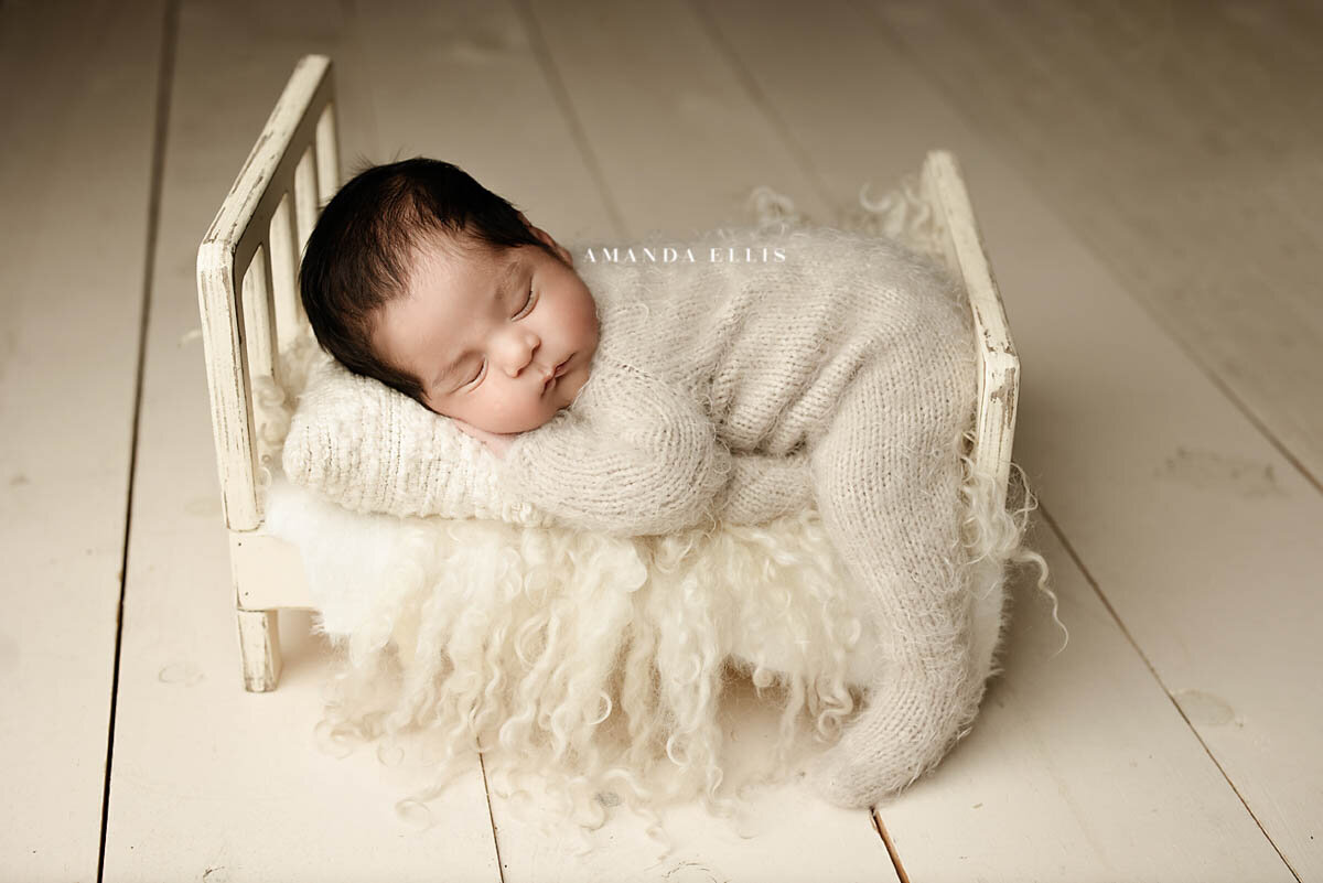 Bright airy portrait of newborn sleeping on miniature bed