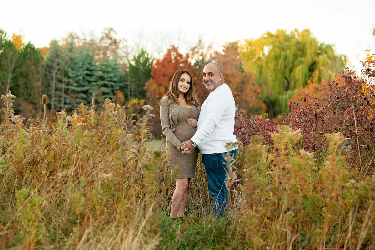 husband and wife facing each other in a field for their fall maternity photography session in Burlington, Ontario 