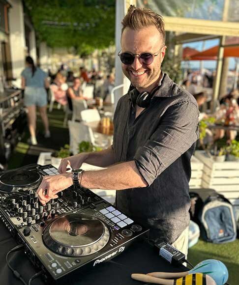 DJ playing music outdoors with Pioneer DJ setup during the sunny daytime at St Kilda Festival