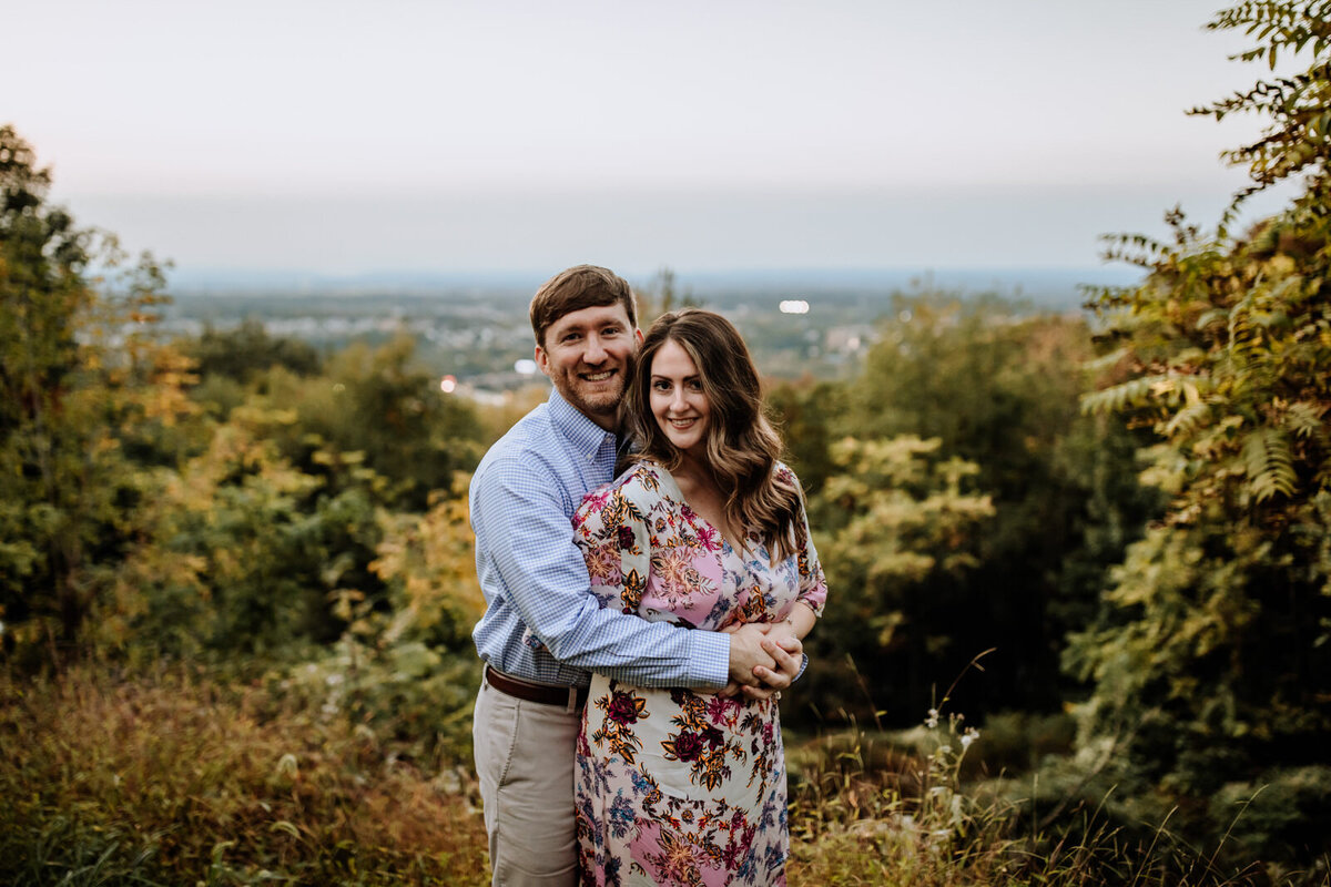 Bride and groom holding hands looking at each other while standing in front of rolling hills with the sunlight coming down on them
