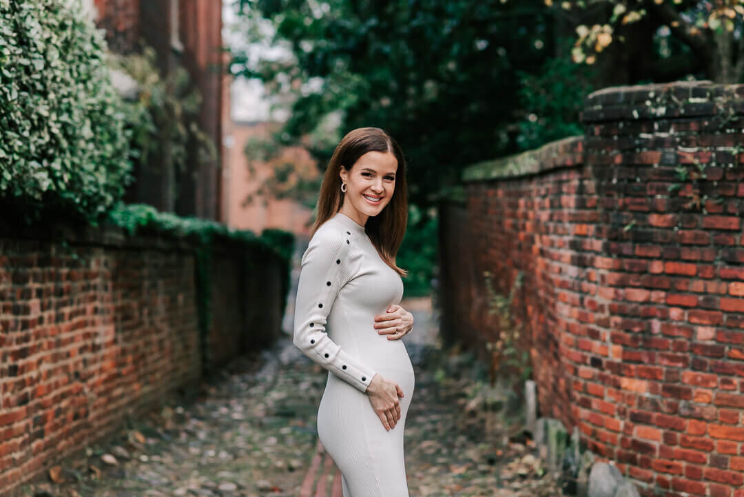A woman holding her bump standing on a cobblestone alley in Alexandria VA
