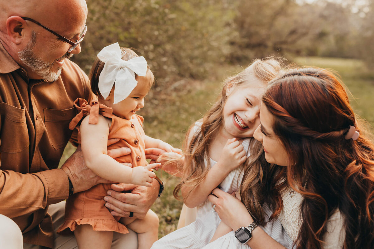 mom tickles daughter while dad holds baby girl on his knee.