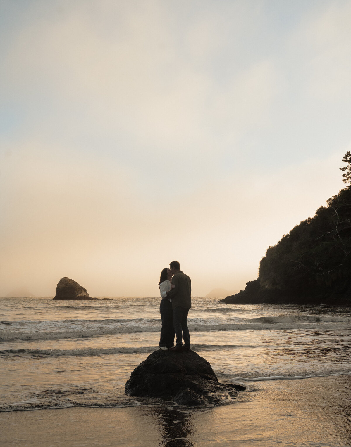 engaged couple silhouetted against golden hour light with wide ocean views in the background