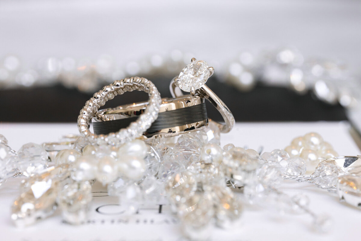 close up of wedding rings at The Adolphus in Dallas arranged with beads and a bridal hairpiece, emphasizing the textures and intricate details of the wedding accessories.