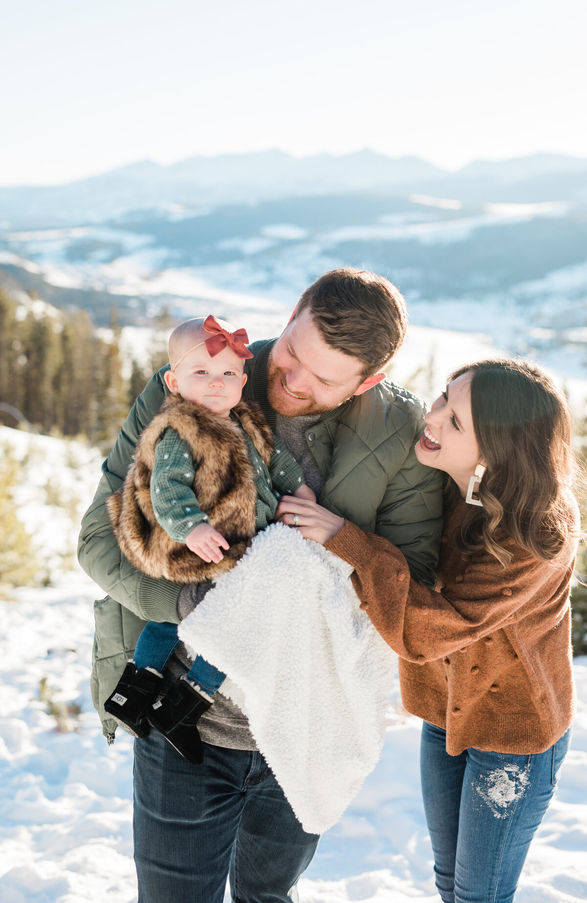 Parents of a young daughter have her bundled up on a winter day. They are posed for a photo