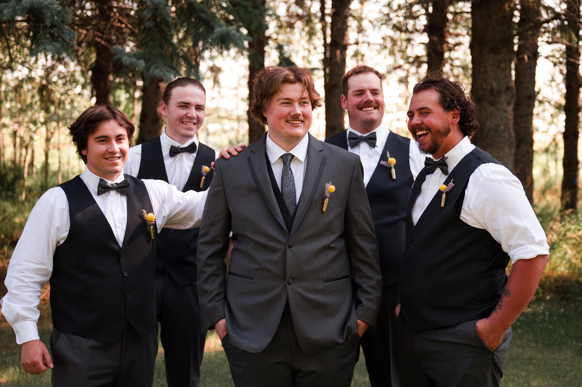 Proud groom standing in the middle with all of his groomsmen around him, all smiling and enjoying the wedding at Falkenberg Stables in Alberta