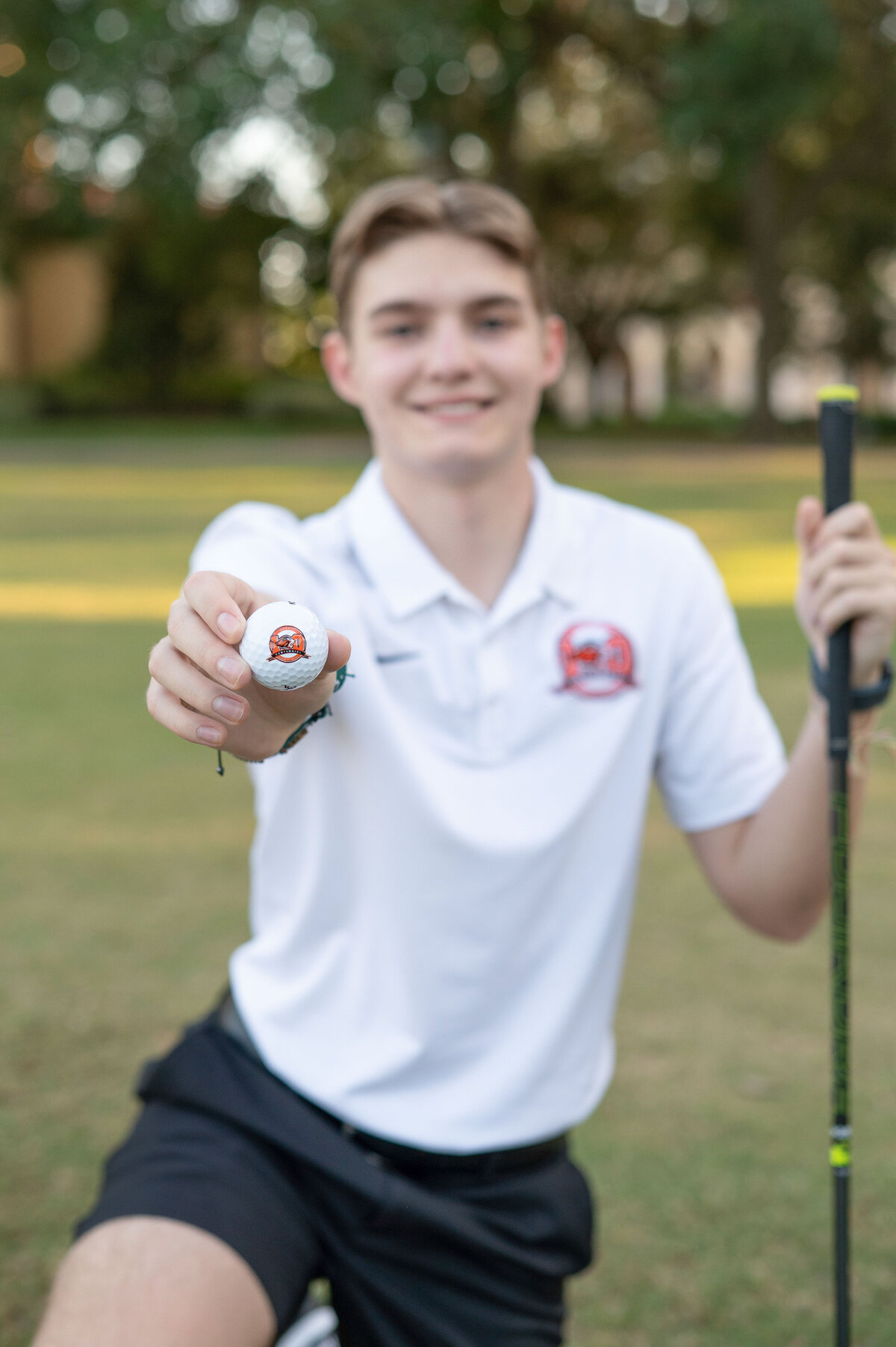 High school senior boy with golf club holding golf ball to the camera.