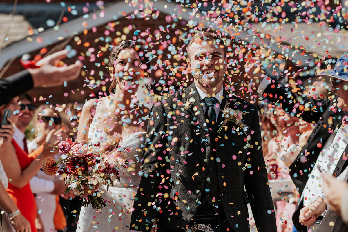 Bride and groom walk through a flurry of multicoloured confetti at King's Chapel, Amersham