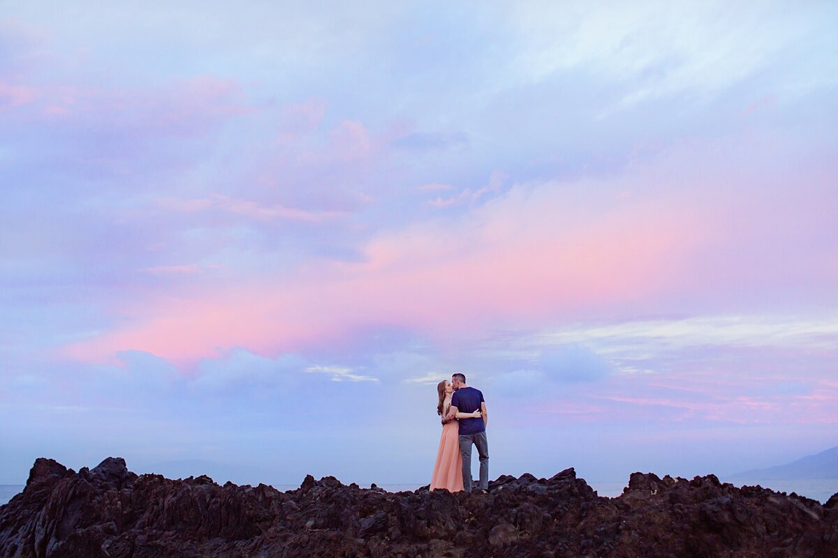 Couple kiss on a lava rock outcrop during their Maui proposal portraits at sunrise.