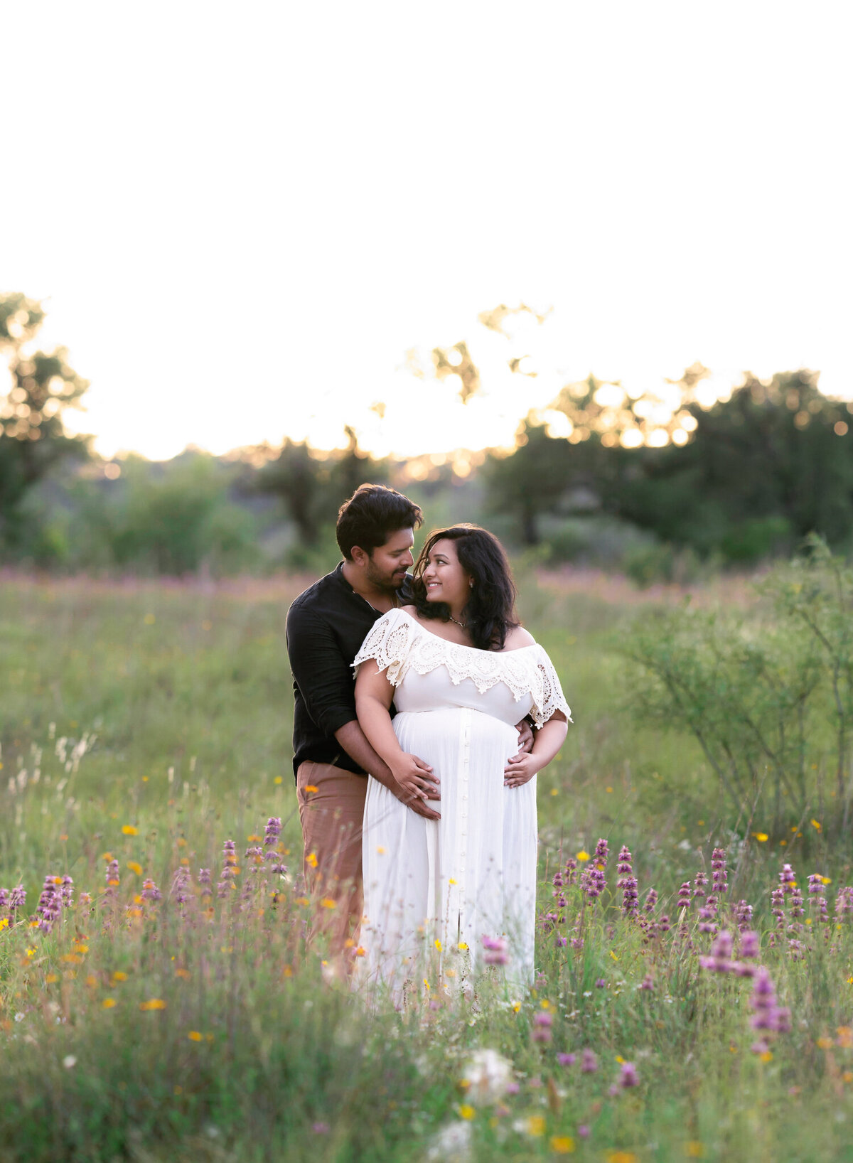 pregnant couple mom in white boho dress dad in black in wildflower field outside of Austin