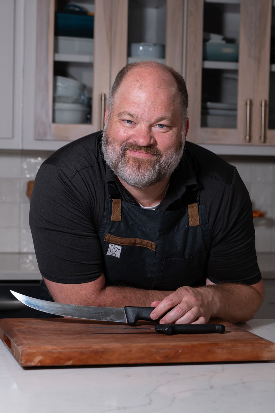 A person leaning over a counter smiling and showing off a knife 