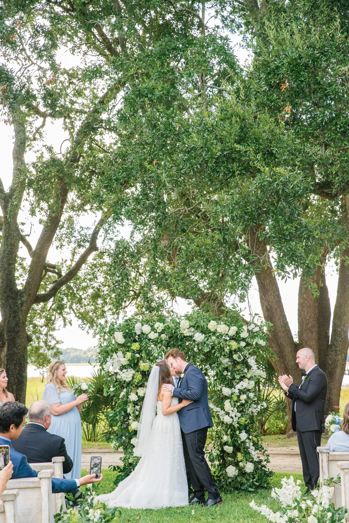 bride and groom's first kiss in front of floral arch at lowndes grove charleston sc