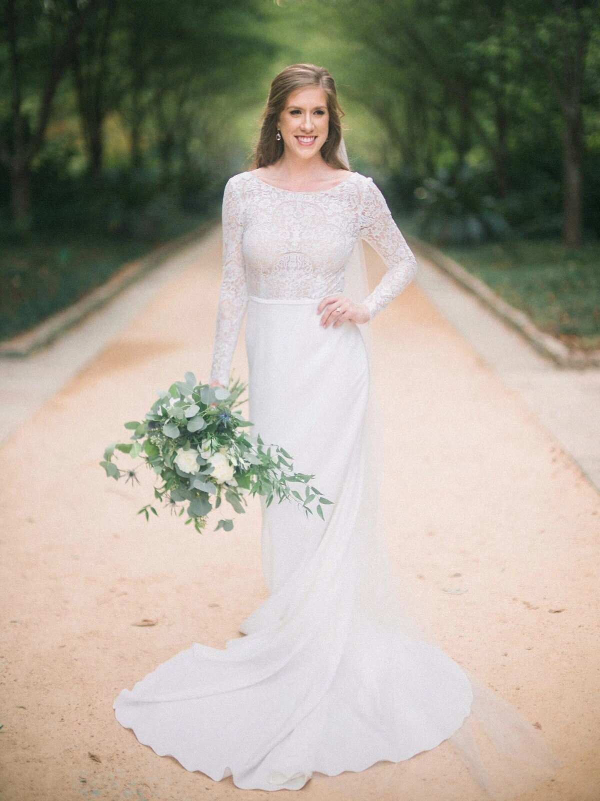 A bride smiling with one hand on her hip and a bouquet in the other