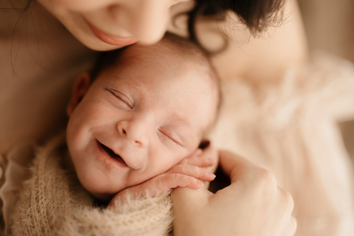 Close up photo of a baby held in his mothers arms and smiling whilst he sleeps