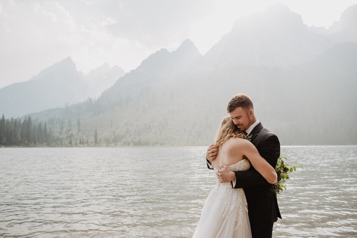 Jackson Hole Photographers capture bride and groom hugging lakeside during adventure elopement portraits