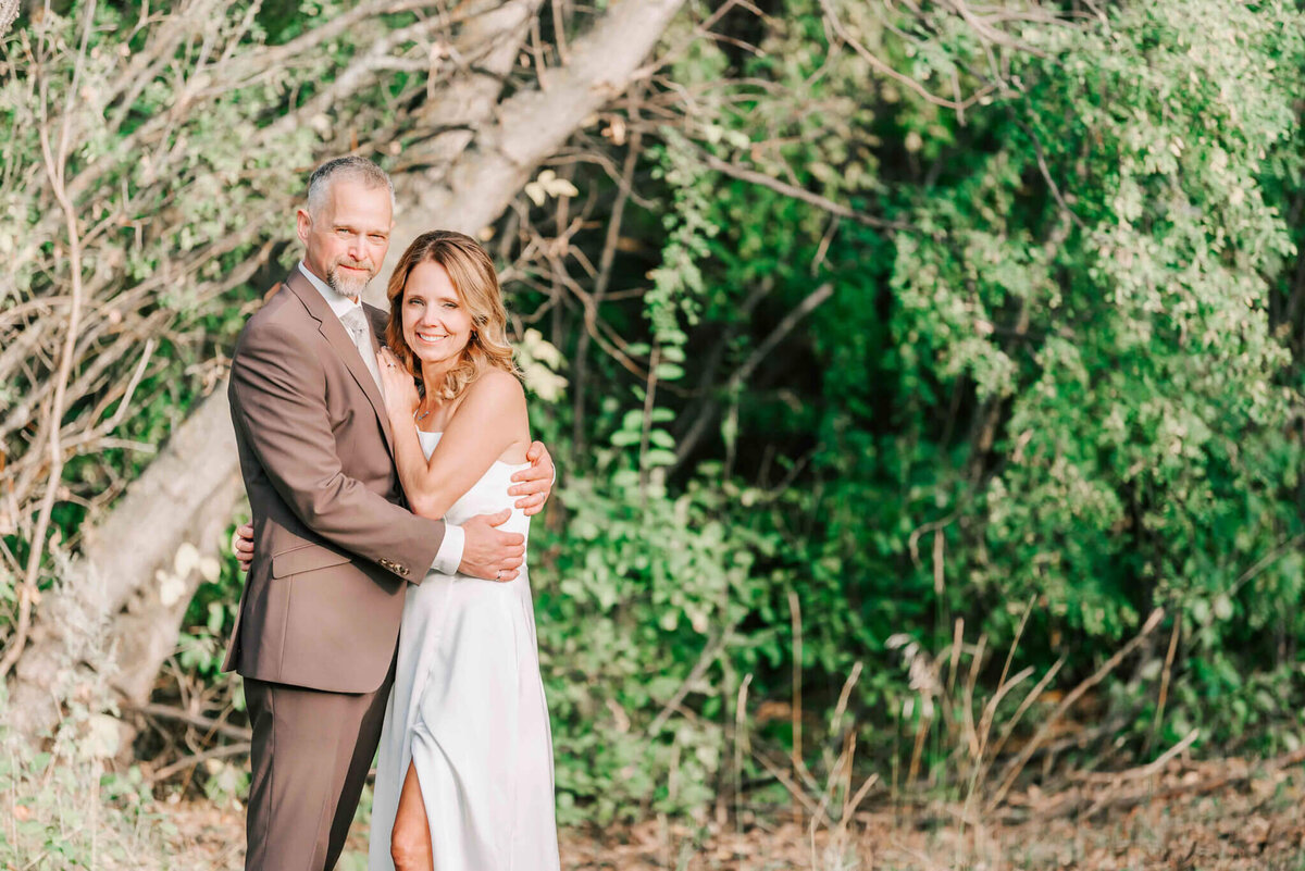 Bride and groom standing towards each other closely. among some trees.