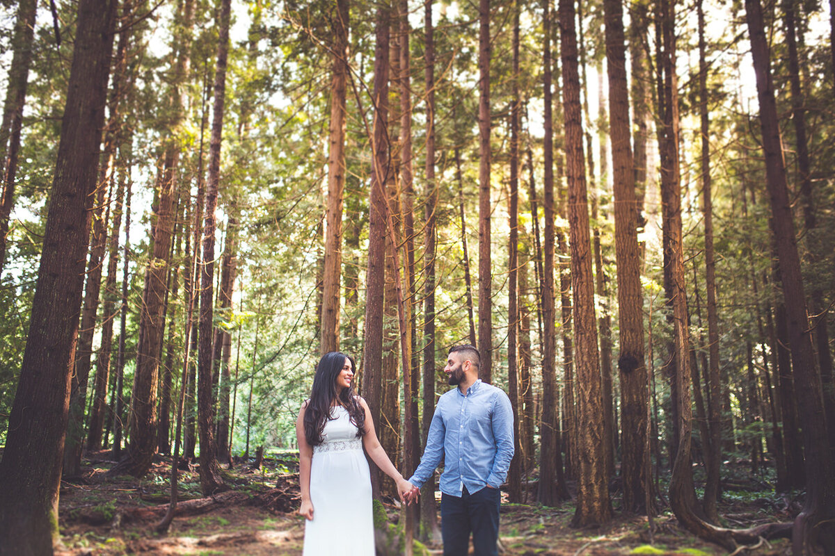 A Vancouver Island couple smiling and holding hands during their engagement session in the forest.