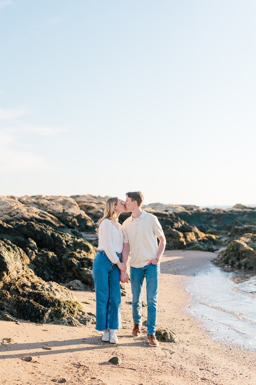 A couple kisses one another in front of rocks at Lighthouse Point Park. 