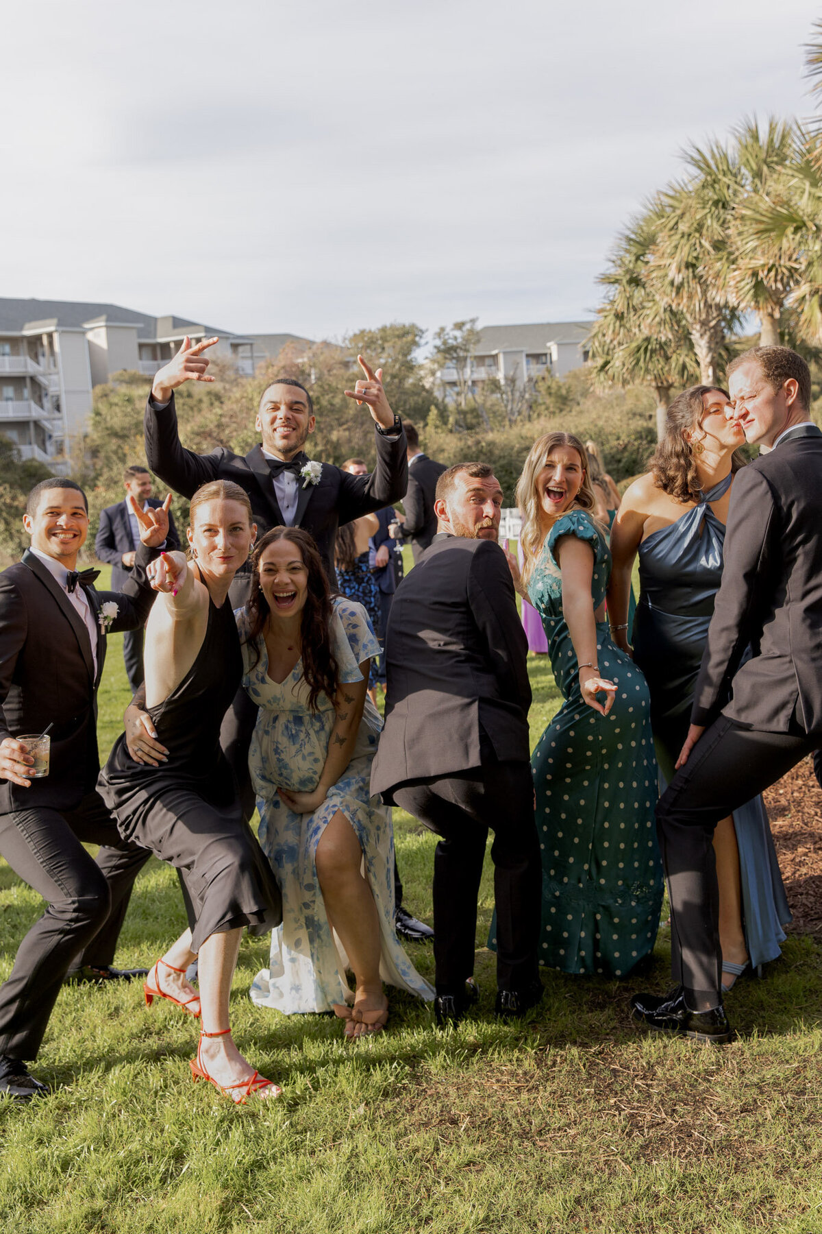 Guests at a wedding all posing for a silly photo. The frame is full of people who are outside at a wedding reception during the day.