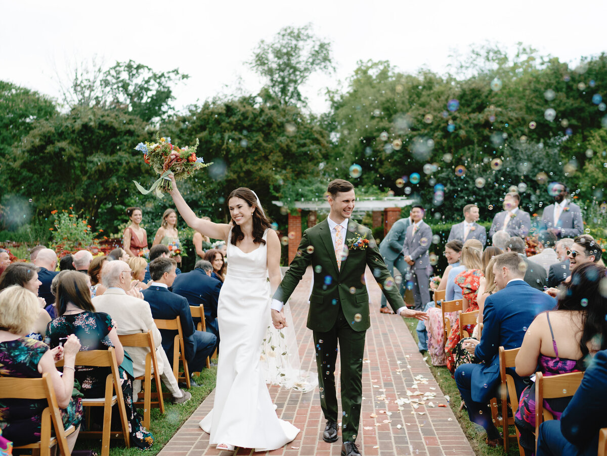Bride and groom walk through bubbles after their wedding ceremony at River Farm