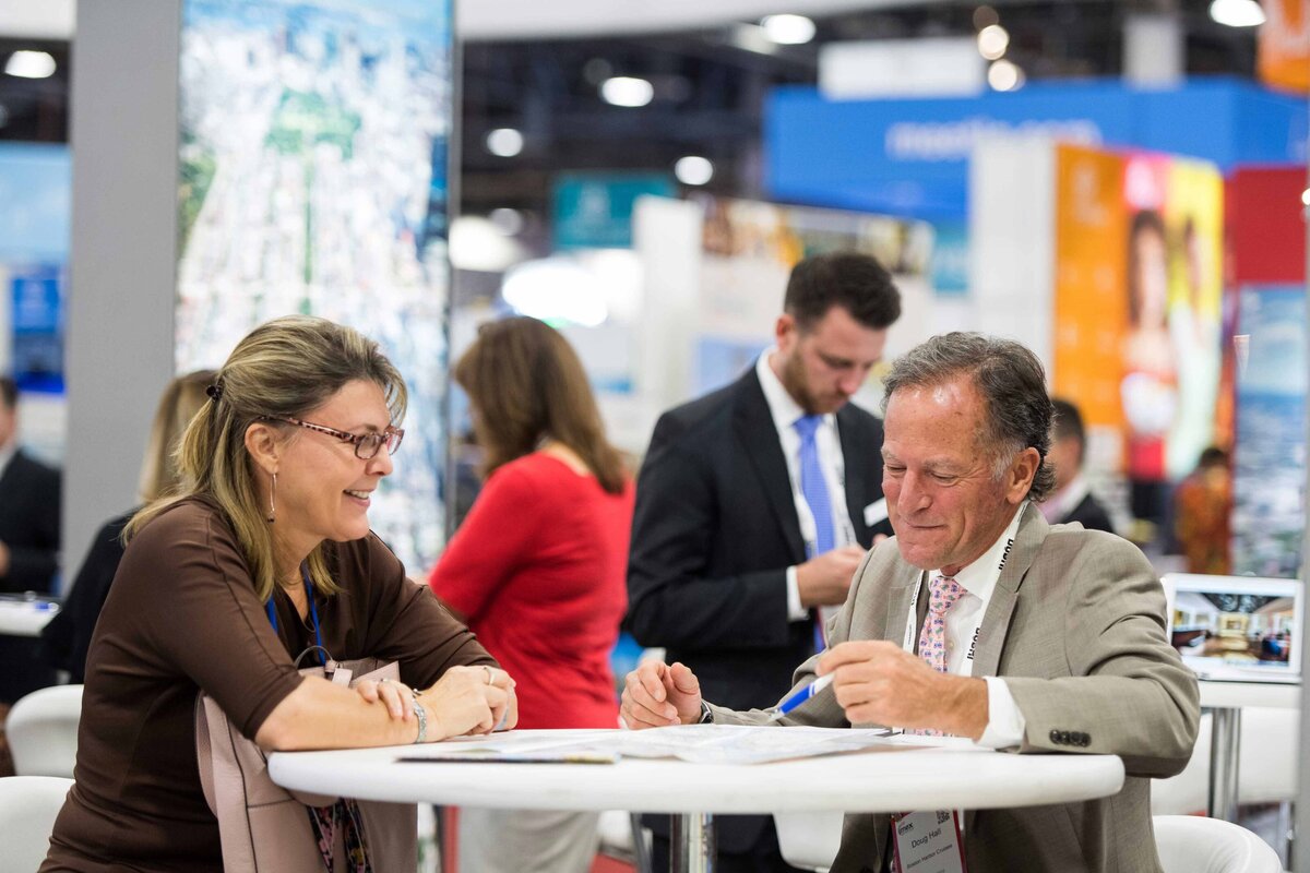 Two sales representatives sit at bellyup table engaged in conversation about offsite events