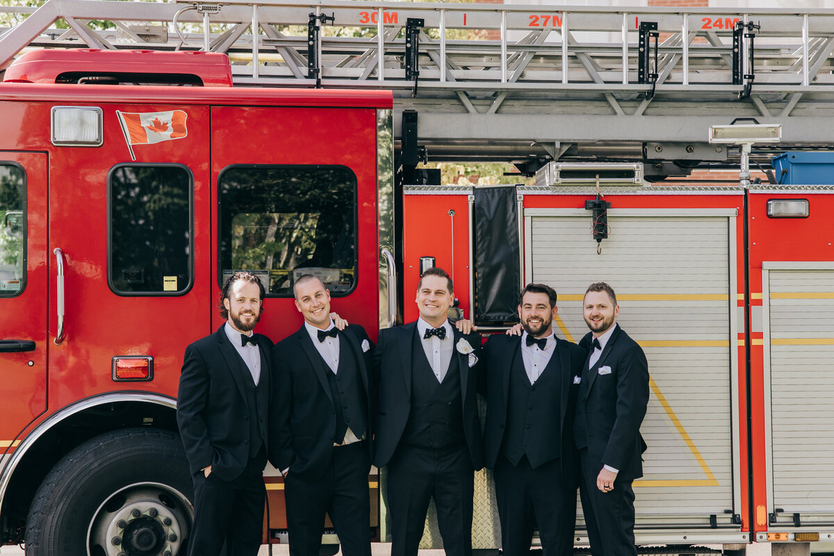 Groomsmen wearing black attire posing for photos in front of a fire truck