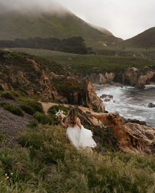 Bride with floral bouquet walking along coastal trail on the dramatic cliffs of Garrapata Beach in Big Sur, CA