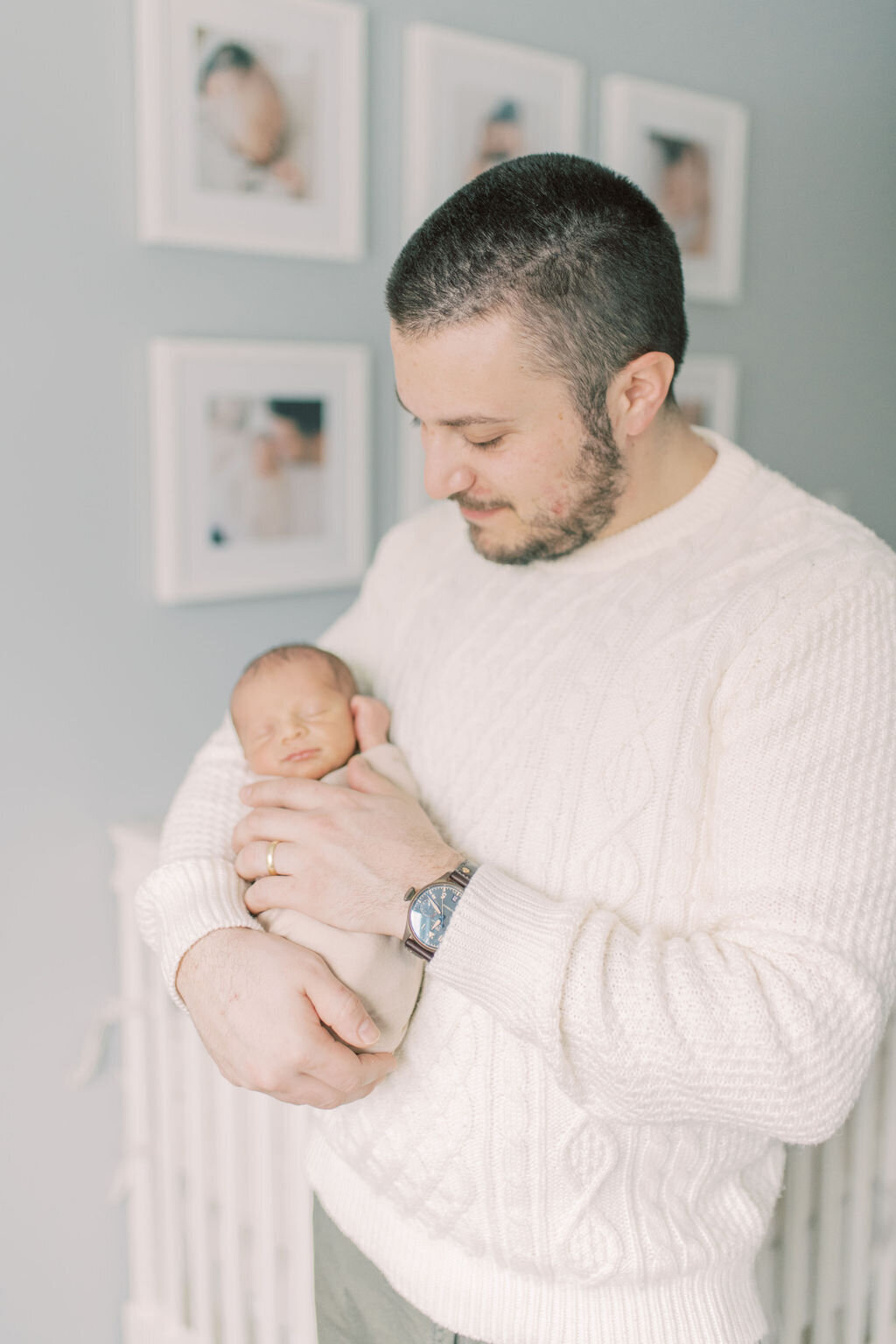 Father holding newborn in front of framed portraits – natural light newborn photography with a personal touch