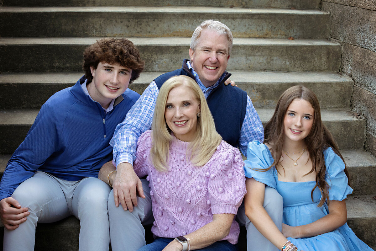 Brilliant Autumn photograph of a family of four seated on concrete steps in South Charlotte NC, coordinated blues and pinks creating a clean, timeless portrait.