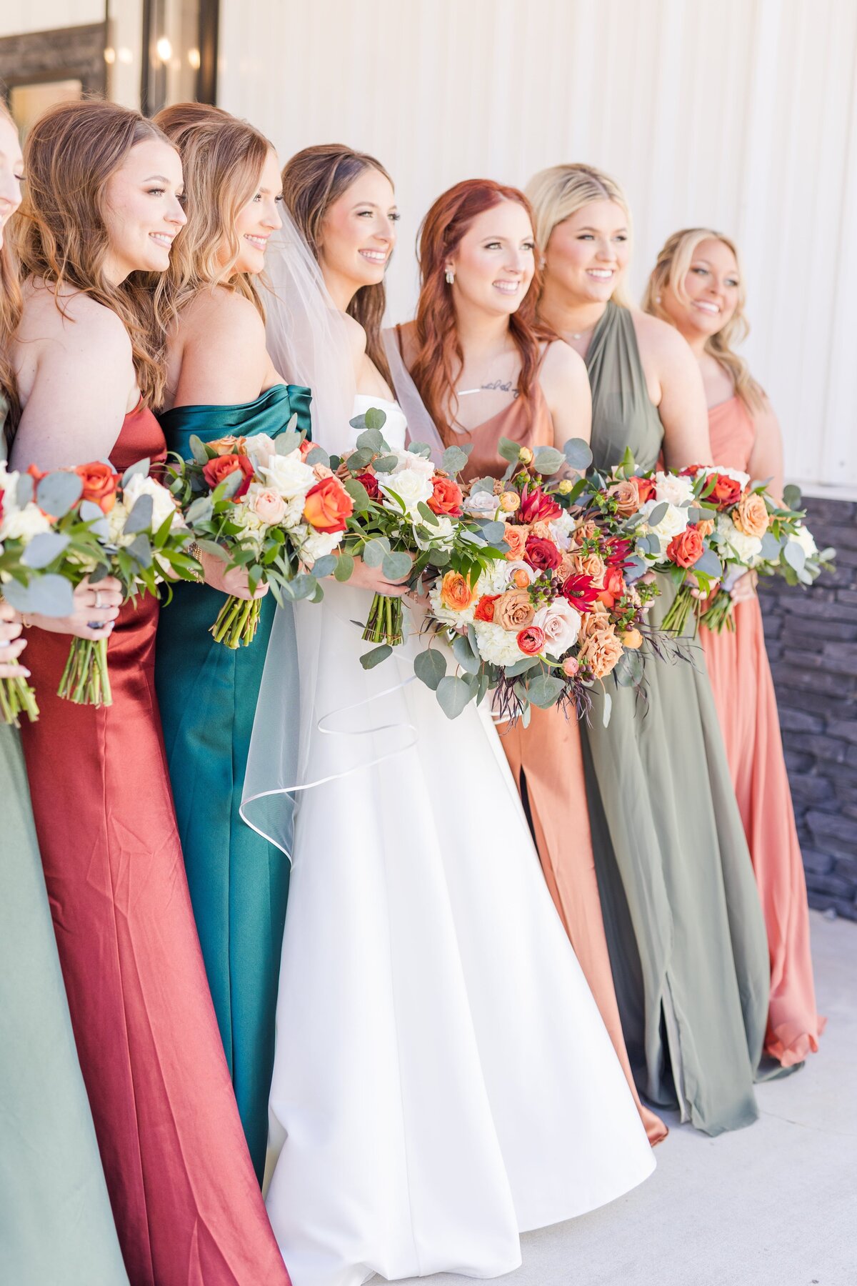A bride stands with her bridesmaids in all different color dresses