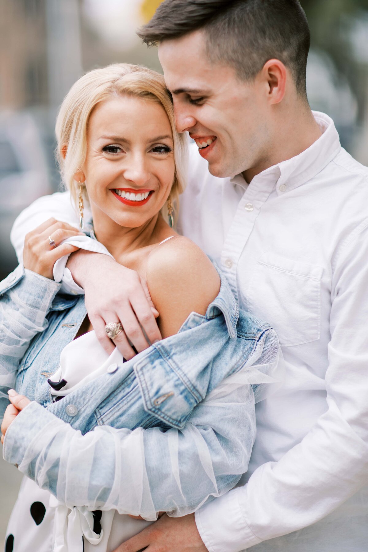 Smiling bride in polka dot outfit is being hugged by groom in a white button down shirt on the streets of Charleston