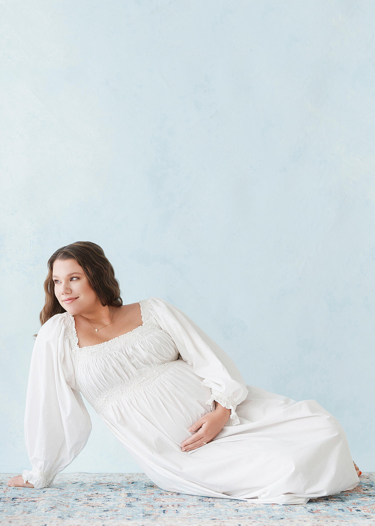 maternity client photographed in brunswick ga studio and she is wearing a white dress on a hand painted blue canvas background