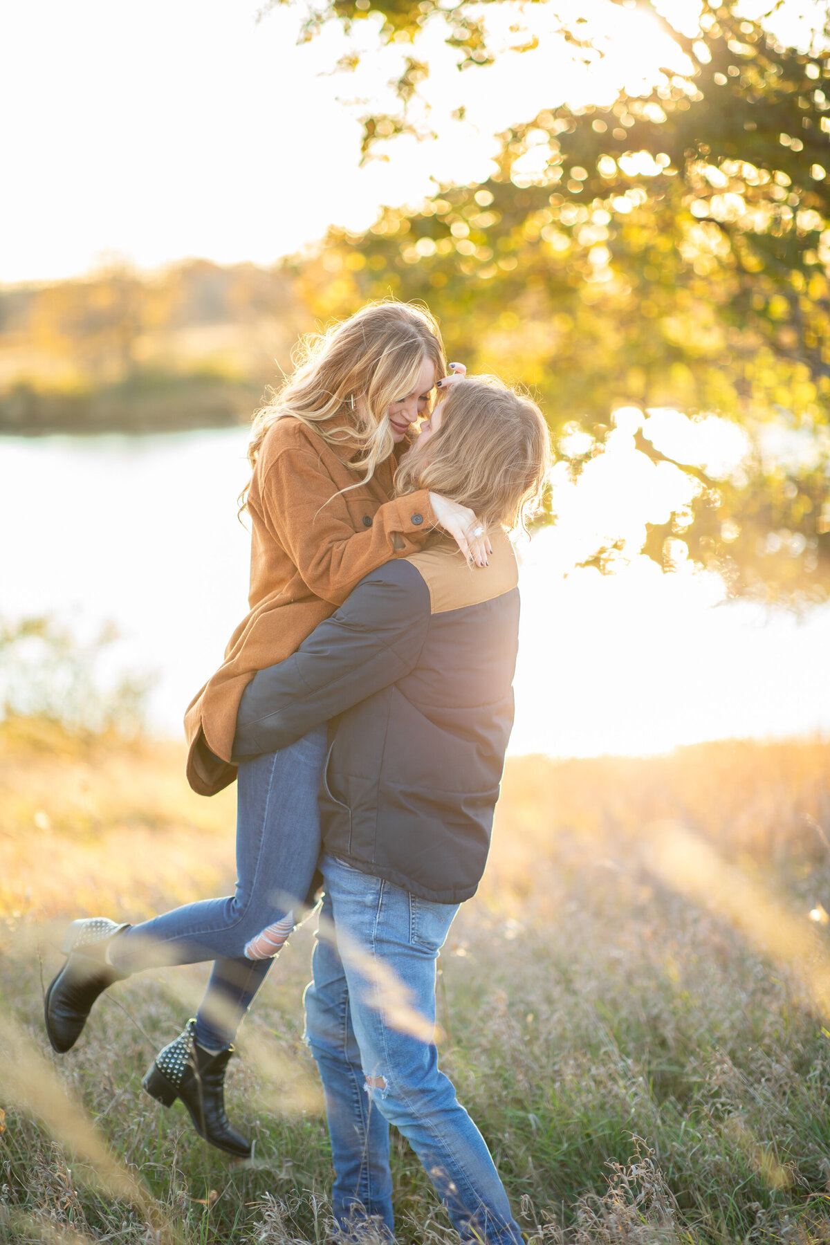 Couple kisses as man lifts up woman by a pond.