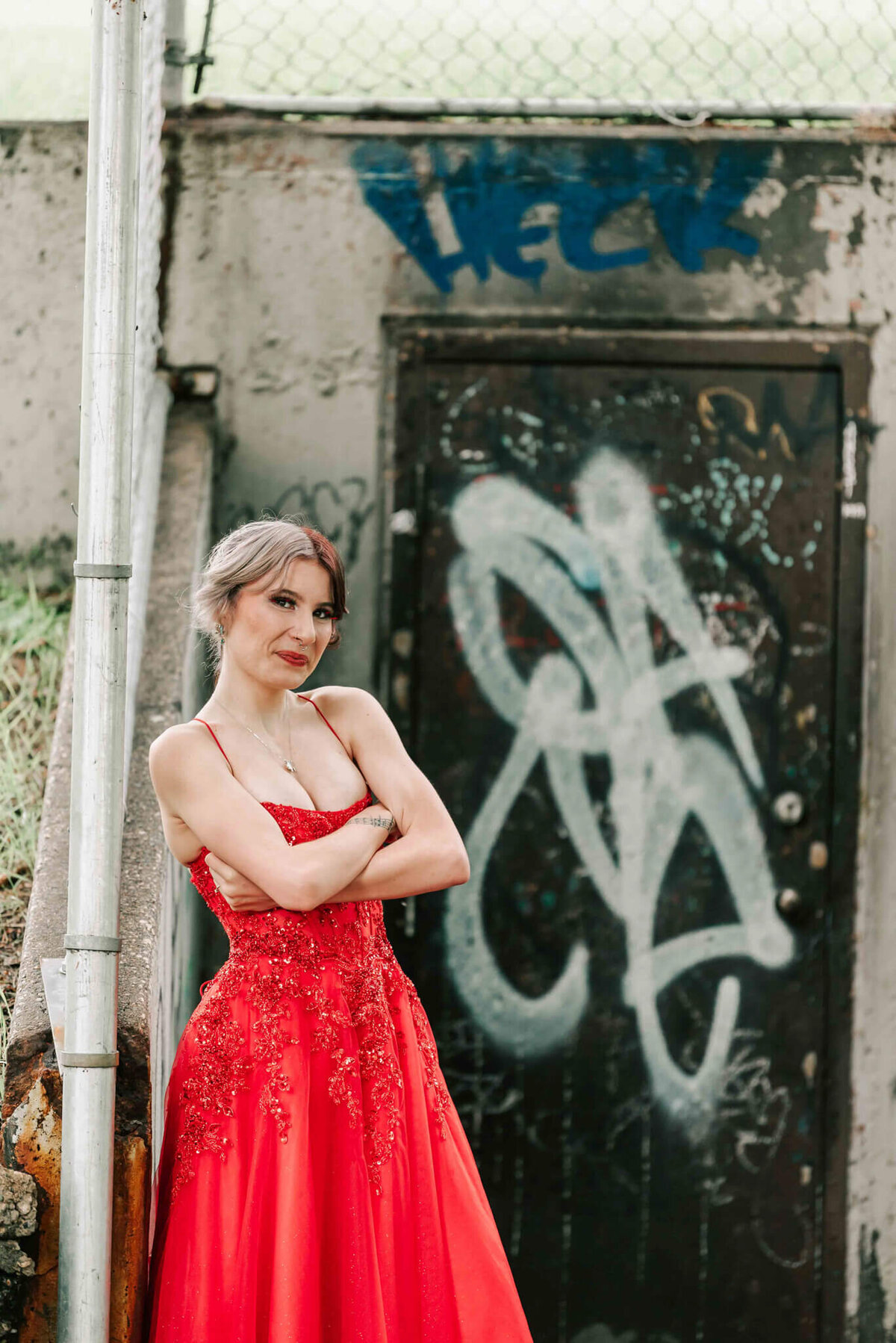 Crossing her arms by a door covered in graffiti.  