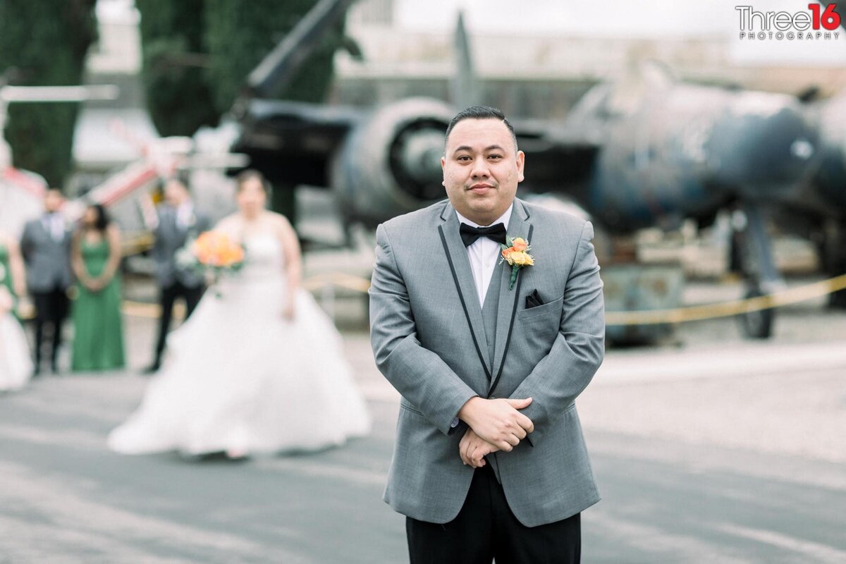 Groom poses for a photo as his Bride sneaks up behind him