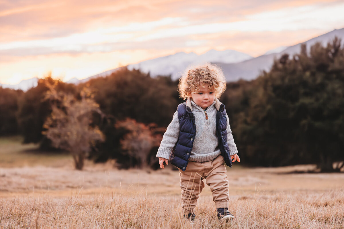 boy walkin in the grass with snowy mountains in wanaka on the background captured by Bie during a wanaka family photography session
