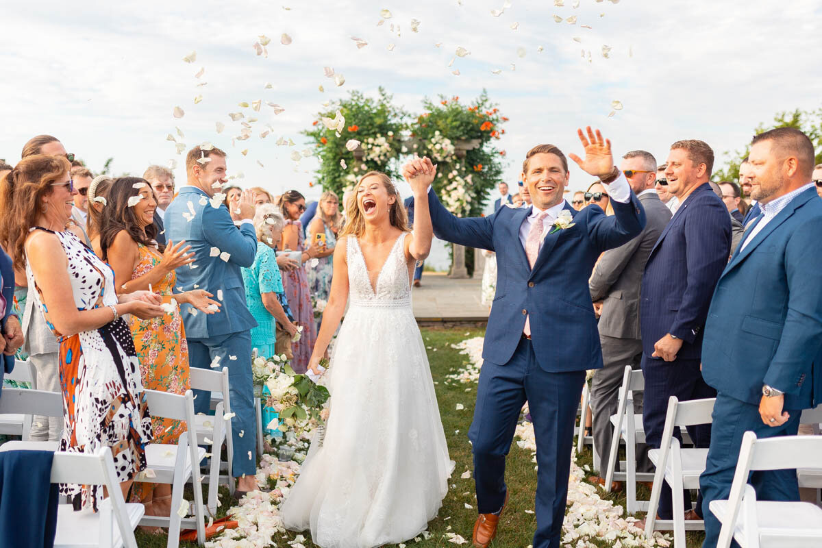 Newlyweds laugh as guests throw flower petals after their ceremony.