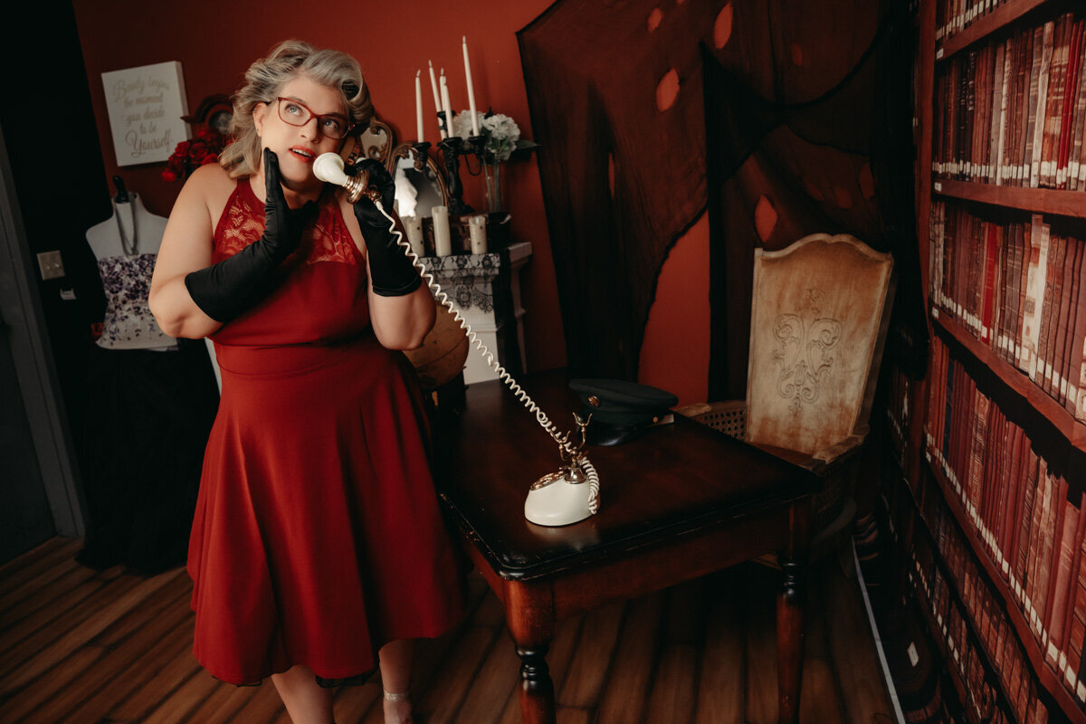 Woman wearing  Vintage red dress  and black gloves  holding the phone in a library set in Minnesota
