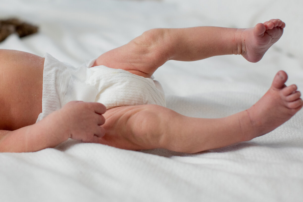 skinny newborn baby legs are extended on a bed