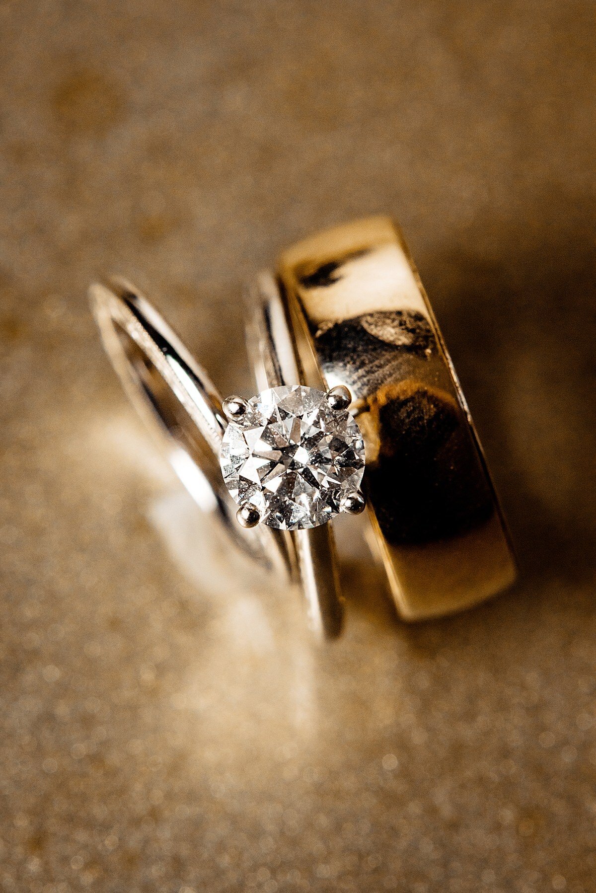 gold wedding bands on a gold background with a diamond solitare engagement ring.