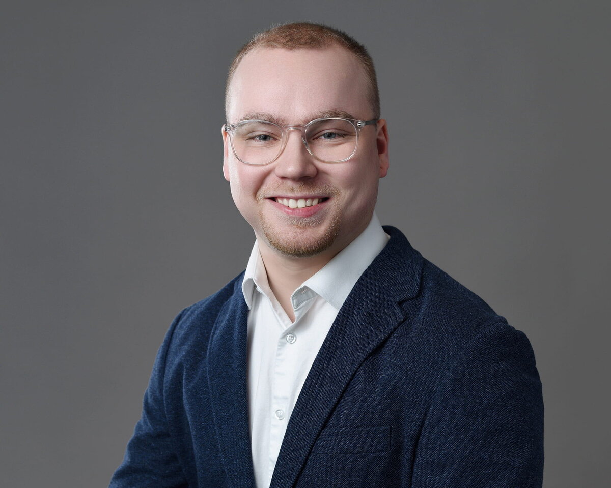 Smiling young professional man in a navy blazer and glasses taken by a Toronto headshot photographer in studio lighting.