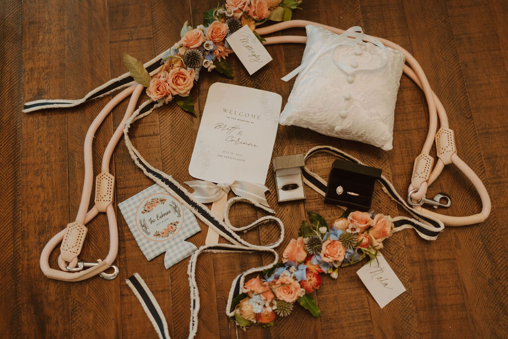 Wedding details including an invitation, rings, flower collar and koozie