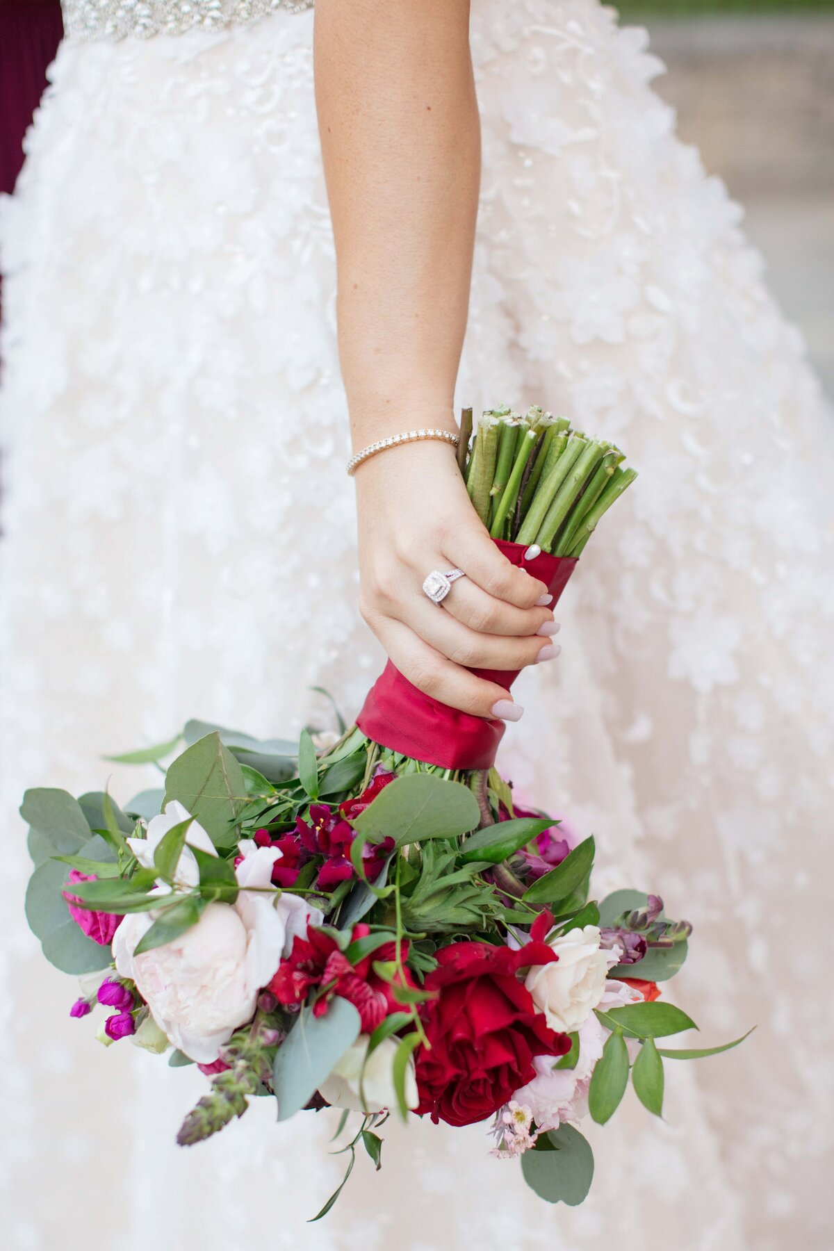 red and white wedding bouquet held at the side of gown showing ring with halo diamonds in New Braunfels Texasby Firefly Photography