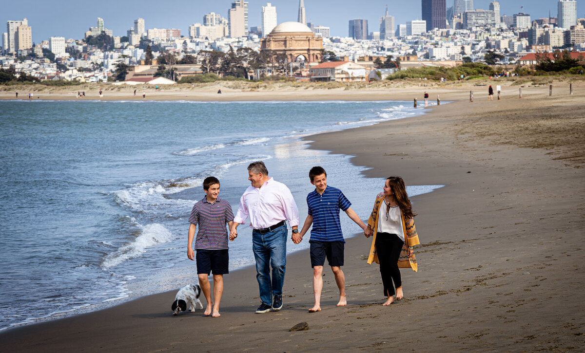 Family of four holding hands on the beach with the city of san francisco in the background