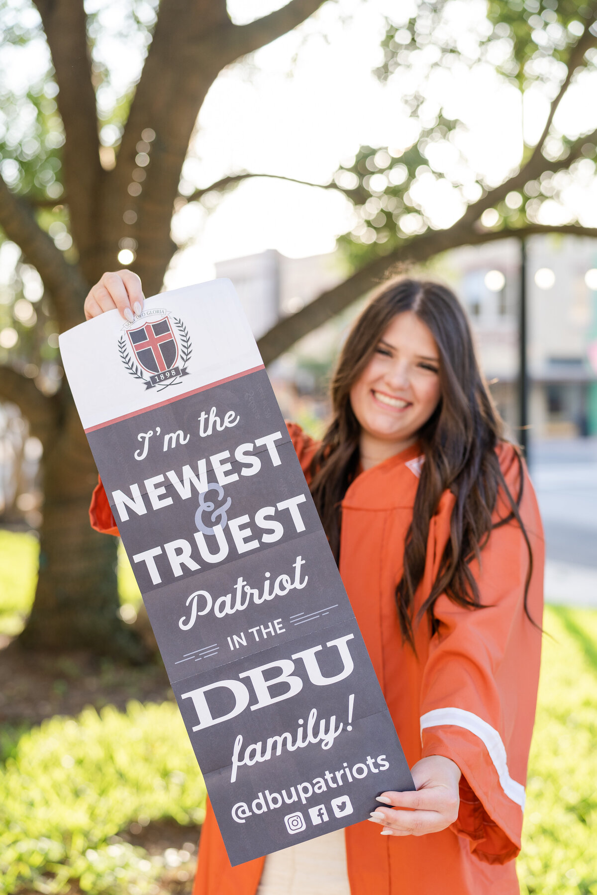 Caldwell High School senior girl wearing gown and smiling while holding out DBU acceptance letter